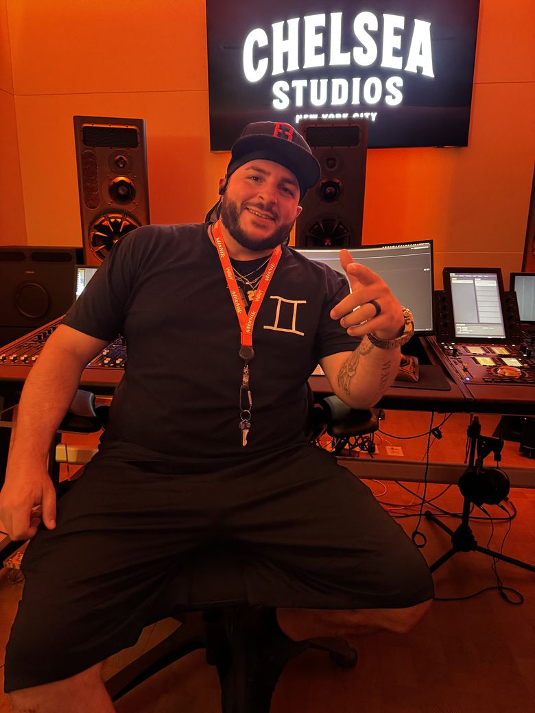 Gemini seated at a mixing console in a studio, pointing at the camera