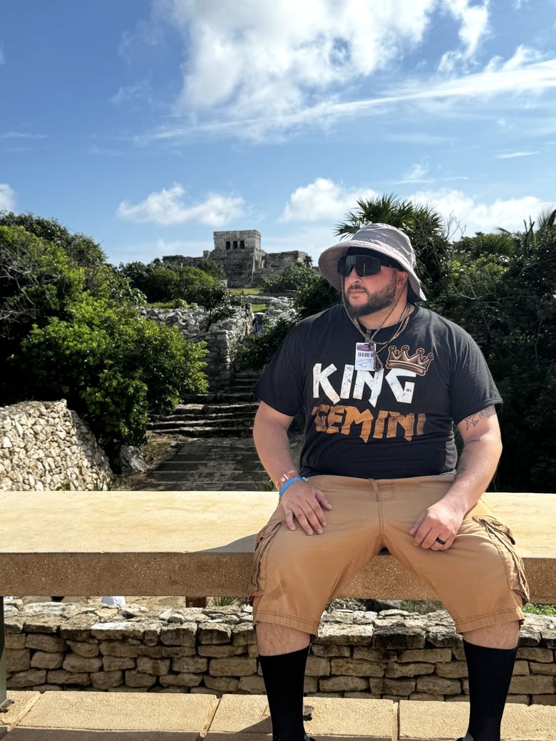 Gemini in sunglasses and a bucket hat wearing a King Gemini tee, seated outdoors